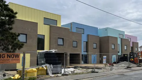 Phil Harrison/BBC Four square houses behind construction fences. Each house is heavily accented with a different colour - yellow, blue, light green and pink.