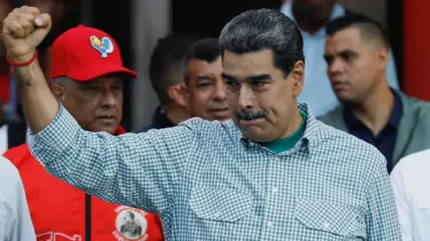 Reuters Nicolás Maduro yang mengenakan kemeja kotak-kotak mengacungkan tangan kanannya. Di belakangnya, Menteri Dalam Negeri Diosdado Cabello terlihat mengenakan jaket merah dan topi baseball merah. 