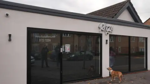Joe Giddens/PA The exterior of Ritzy barbers shop, which is mostly large floor to ceiling windows between a beige front. It looks quite smart. A dog stands outside looking at the shop.
