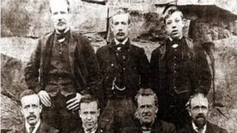 Supplied An old black and white image of seven men, wearing old fashioned suits.