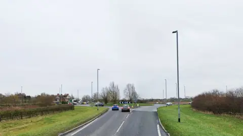 Google street view showing the approach to the Partney roundabout on the A158. Two cars are in the left hand lanes just about to drive on to the roundabout.