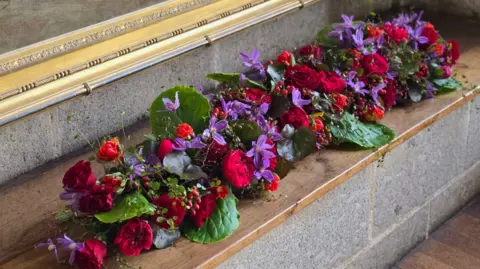 A floral display in various colours on a wood and stone platform.