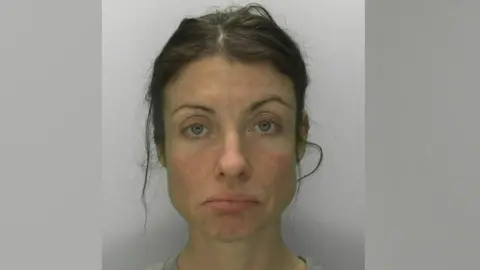 Mugshot of Emily Dixon, a 39-year-old woman with brown hair scraped back messily and a big frown