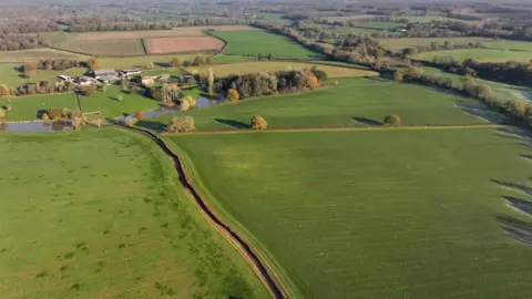 Eddie Mitchell Large green fields with farm buildings in the background 