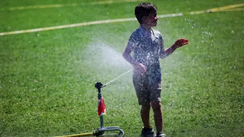 Andy Rain/EPA/Shutterstock A young boy cools off at a grass sprinkler on a hot summer day at Parliament Square in London.