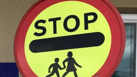 A generic yellow and red circular school crossing 'lollipop' sign with the world 'STOP'