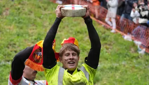 A man holding a wheel of cheese above his head
