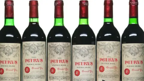A row of six red wine bottles. The labels on them say "PETRUS"
