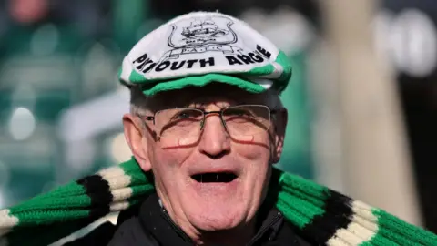 Reuters A picture of an man with glasses, grey hair and wearing a green scarf.