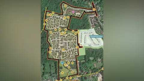 An aerial view of a housing development. It is surrounded by trees and fields. 