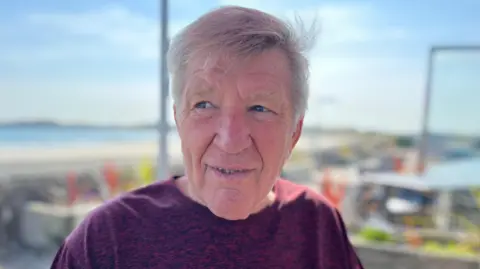 A grey haired man with a purple T-shirt.