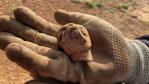 A decorative flagon in the shape of a woman’s head being held in the open palm of a person's hand.