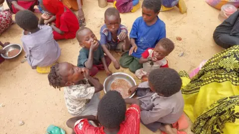 Children sit around a bowl and eat in Darfur