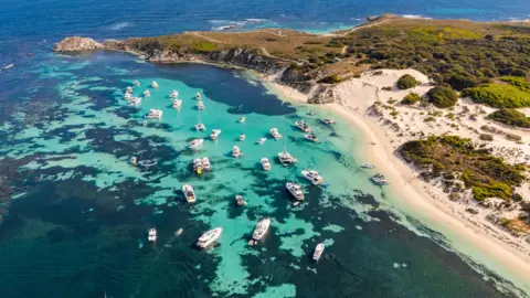 Aerial view of Rottnest Island, with turquoise waters and a sandy coastline and grassy hills