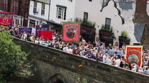 Getty Images An aerial photo of people marching as part of a previous Miners' Gala. They're walking across a stone bridge with various colourful banners.