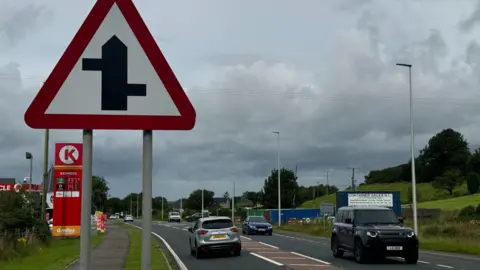 A picture of the A5, with a road sign on the left hand side, and cars on the road. There is a petrol station on the left hand side.