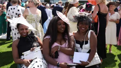 NEIL HALL/EPA/Shutterstock Three ladies huddle together on the first day of Royal Ascot.