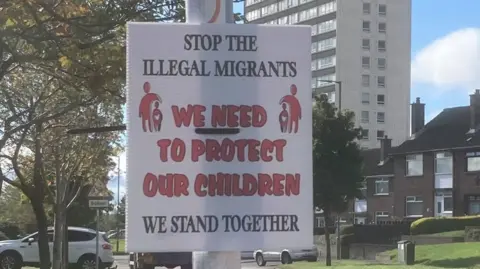 A poster that says 'Stop the illegal immigrants, we need to protect our children. We stand together.' in black and red writing with a graphic of an adult and child on either side of the writing.