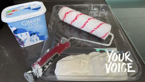 Emma Kent A paint roller next to a tub of Greek yoghurt