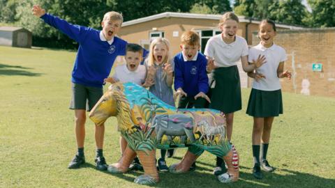 Kids pulling a "roaring" pose behind a lion sculpture