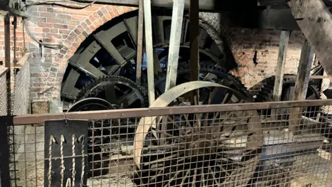 David Spereall/BBC A large water wheel within a well-lit stable house.