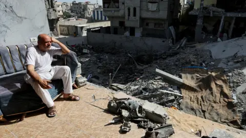 Reuters Een man zit in een ingestort gebouw nadat een Israëlische militaire operatie vier gijzelaars heeft gered die door Hamas werden vastgehouden in het vluchtelingenkamp Nuseirat, centraal Gaza (15 juni 2024)