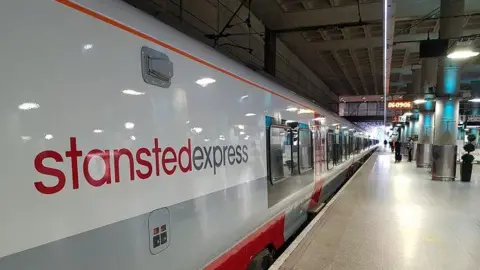 A white and grey train at a platform with the words "Stansted Express" on the side.