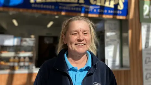 Alex Dunlop/BBC A woman in a blue polo shirt and a black fleece. She has blonde hair and is smiling.