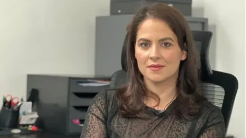 Claudia Alves, an advocate for the Portuguese community is pictured in an office chair wearing a black top.