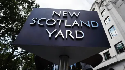 The New Scotland Yard sign, with silver letters on a black background mounted on a rotataing pole, outside the headquarters of the Metropolitan police in central London. 