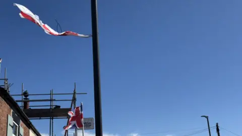 Union flags flutter from lamp-posts on a sunny day with bright blue skies.