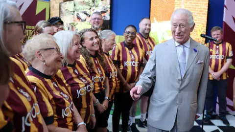 PA Media A picture of a number of people wearing Bradford city football shirts. They are stood in a row next to the King. He is wearing a grey suit.
