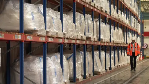 BBC / Tracey Langford One tonne sacks of rare earth metals lines the shelves of a warehouse as they wait to be shipped off to customers