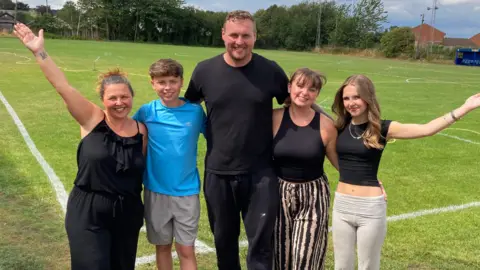 The Stockdale family from left to right - Katie, Billy, David, Mollie and Daisy - are standing on the pitch at Farsley FC with their arms around each other
