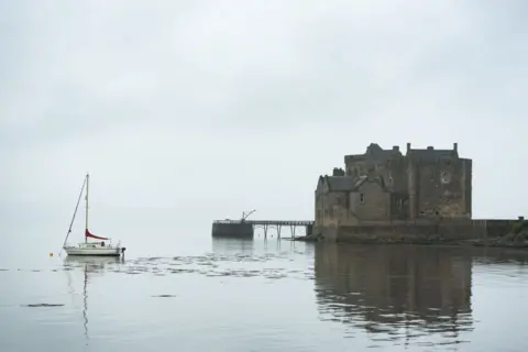 Ania Ciolacu Landscape of a boat in the water with a castle in the background on a foggy day