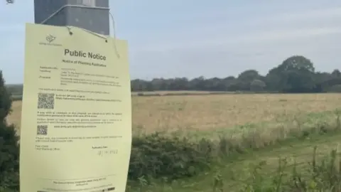 A large field with a pole in front of it with a public notice stuck to the front