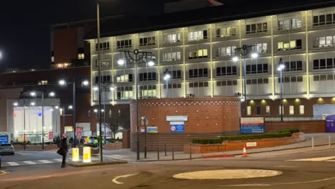 A multistory hospital building. The image was taken at night, with windows lit up. 