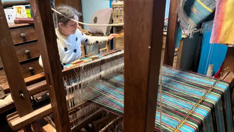 bbc A woman sits at a loom