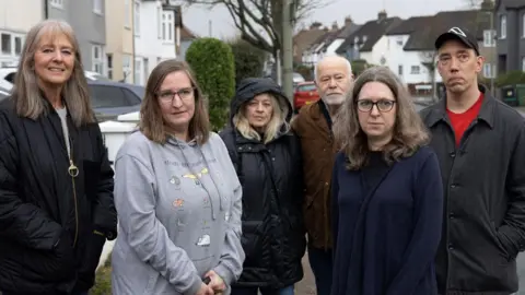 Facundo Arrizabalaga/MyLondon A group of six people - four women and two men - standing in a row in a residential road, looking at the camera 