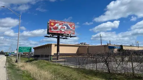 Billboard with two hands making a heart, one hand has the Canadian flag and the other has the American flag. The sign reads "Two nations, One Love".