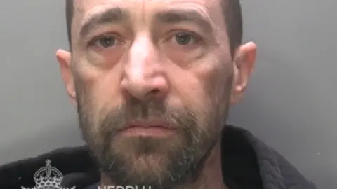 Mugshot of a man with a bald head and beard
