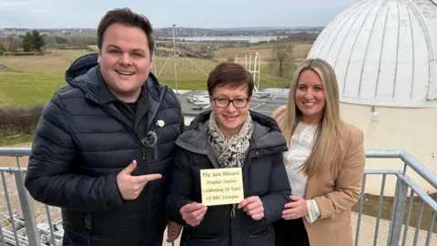 BBC weather presenters Rob Rose, Sara Blizzard and Anna Church on the balcony of a planetarium with Sherwood Observatory in the background.