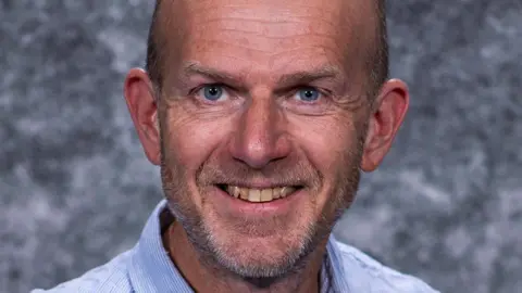 Professor Robert Johns smiling in front of a plain grey background
