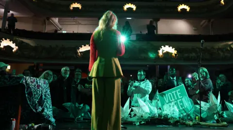 EPA Green Party winning candidate Hannah Spencer addresses supporters during an election after-event after the vote count. They are in an old theatre with people standing in front of the stage and in the tiered seats area