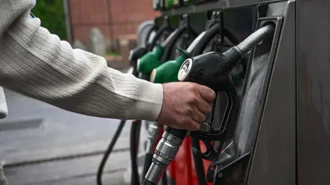 A man grabs a black fuel pump at a petrol station