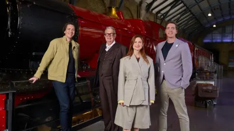 PA Media Four Harry Potter actors on the set of the first film in the series - Harry Potter And The Philosopher's Stone. They are on a platform next to a red steam train. There are three men and one woman.