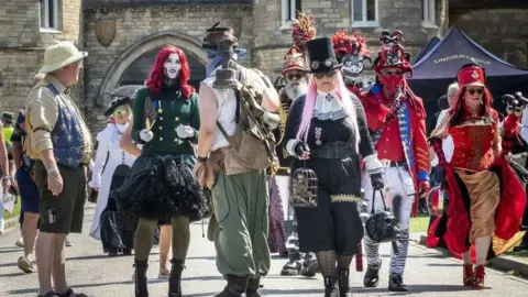 Danny Lawson/PA Steampunks walking through Lincoln's historic quarter. Outfits range from black to red, with some wearing brightly-coloured wigs, or top hats and goggles