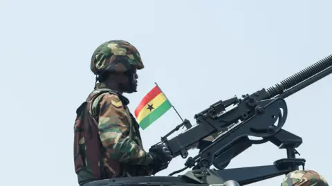 A soldier mans a gun with a Ghanaian flag attached to it