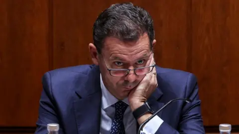 Portugal braced for mass disruption in first general strike for 12 years EPA A man in a blue jacket and tie peers over his glasses while sitting against a wooden background