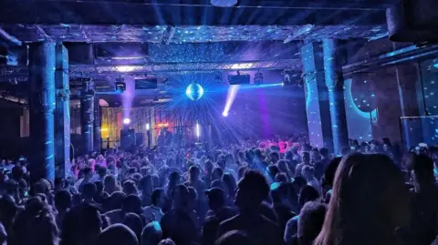 The Underground Hundreds of people enjoy a dance event at The Underground in Bristol. They are illuminated by blue and white lights and light beams are shooting out from a glittering disco ball